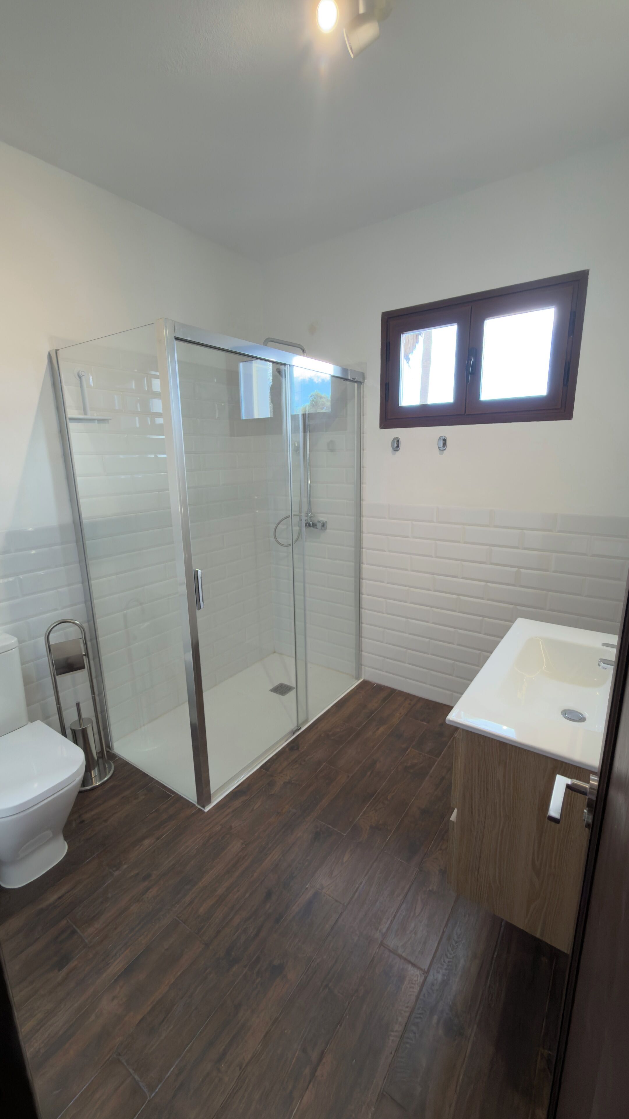 A bathroom with a glass shower enclosure, a toilet, and a sink with a wooden cabinet.