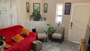 Un salon avec un canapé rouge, des fauteuils beiges, une table basse et une plante en pot.