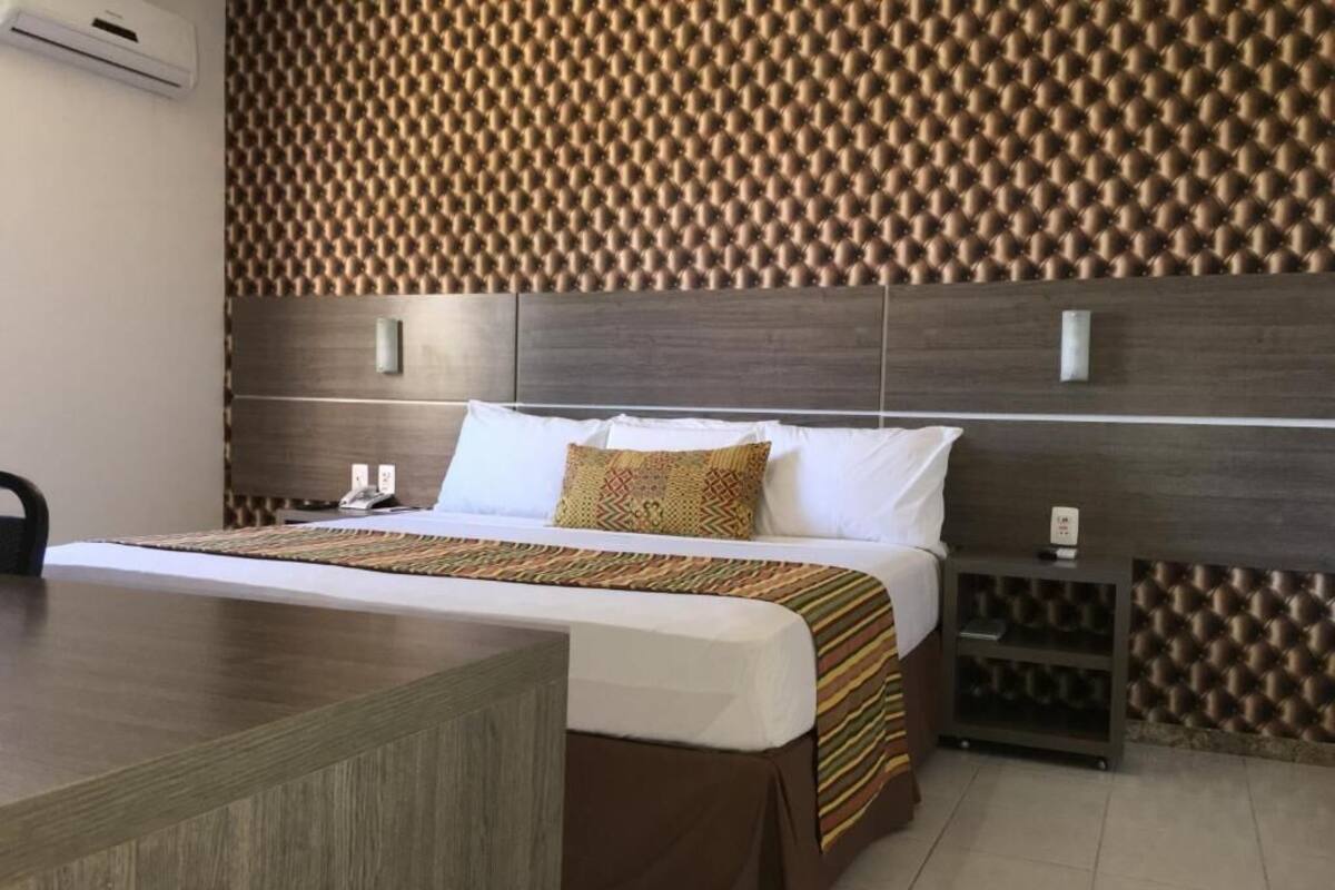 A hotel room with a bed, bedside tables, a desk, and a patterned wall.
