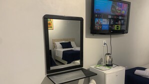 Een hotelkamer met een bed, een nachtkastje met een waterkoker, een spiegel en een tv aan de muur waarop diverse streamingdiensten worden weergegeven.