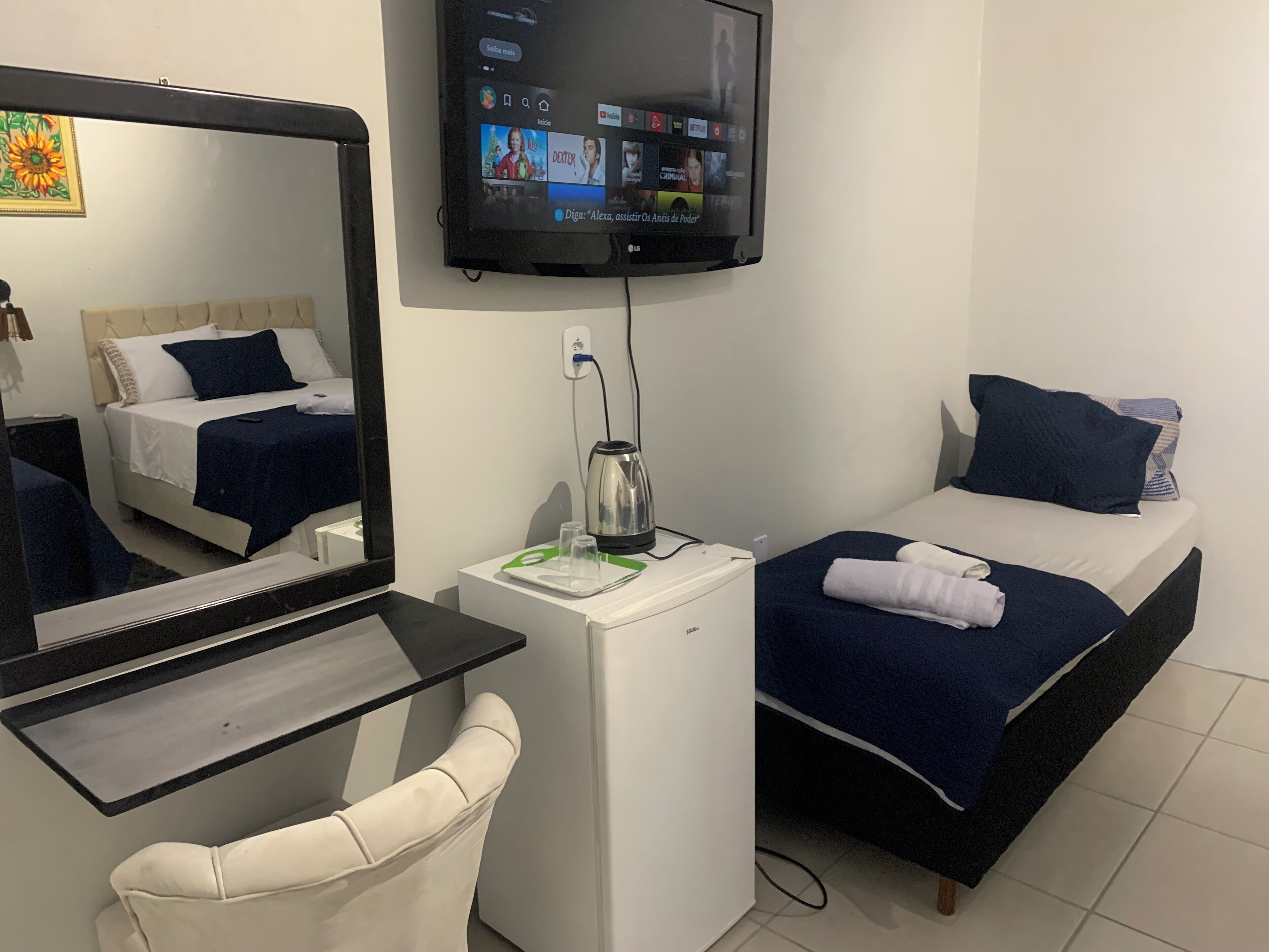 A hotel room with a bed, a desk with a computer, a coffee maker, and a TV mounted on the wall.