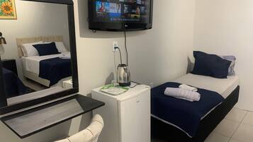 A hotel room with a bed, a desk with a computer, a coffee maker, and a TV mounted on the wall.