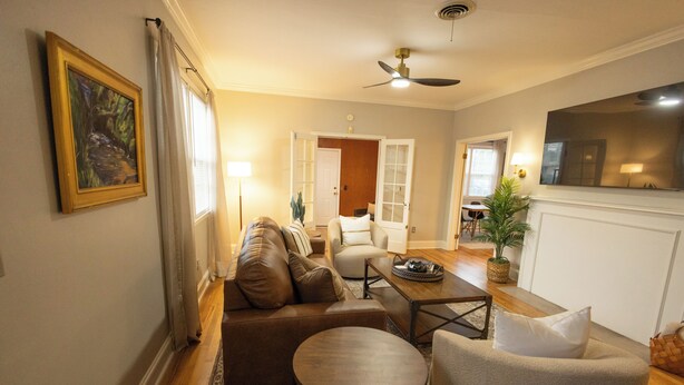 Un salon avec un canapé, un fauteuil et une table basse. Il y a un tableau au mur et un ventilateur de plafond.