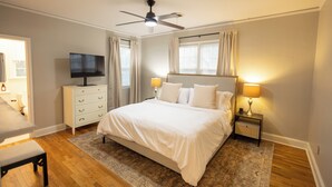 Une chambre à coucher comprenant un lit, un téléviseur, un ventilateur de plafond et une table de chevet avec une lampe.