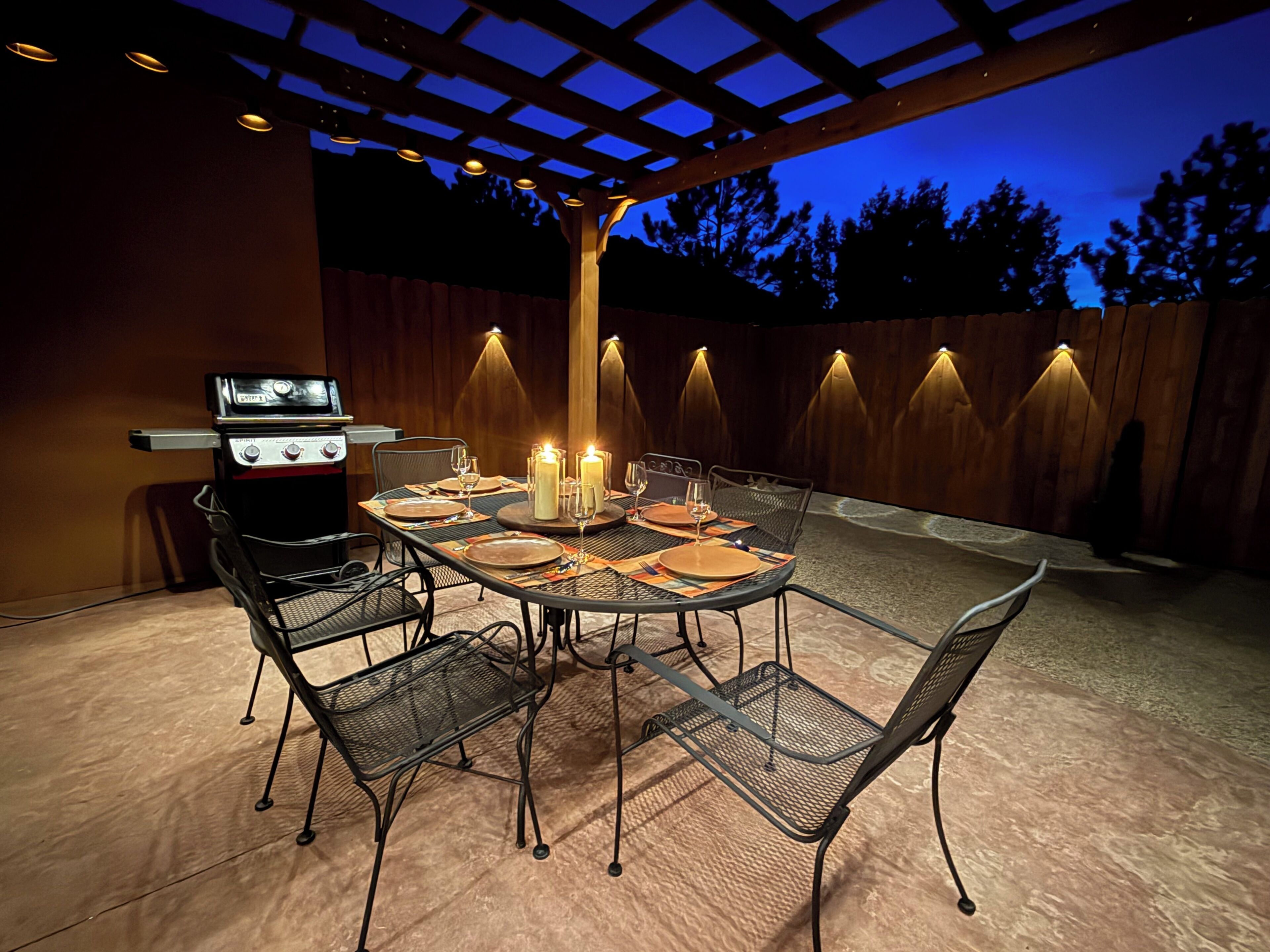 An outdoor patio with a grill, table set for dining, and ambient lighting.