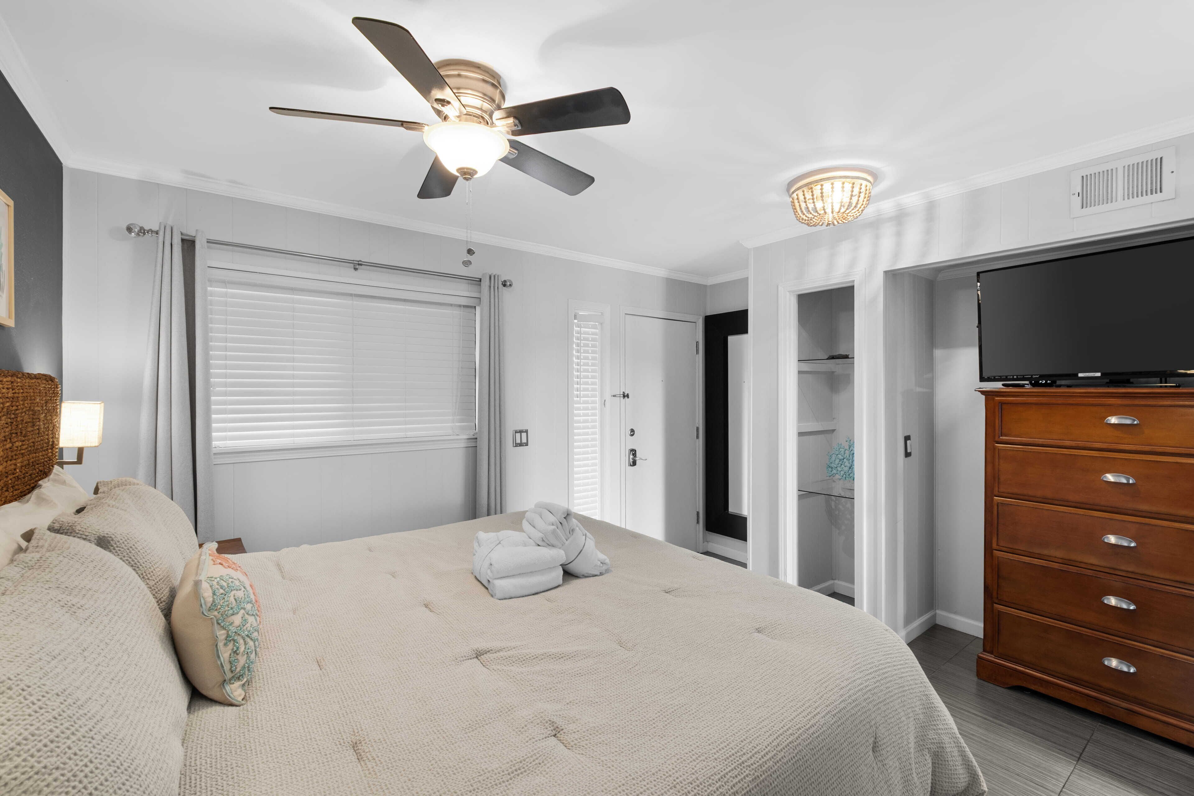 A bedroom with a large bed, a ceiling fan, a TV, and a wardrobe.