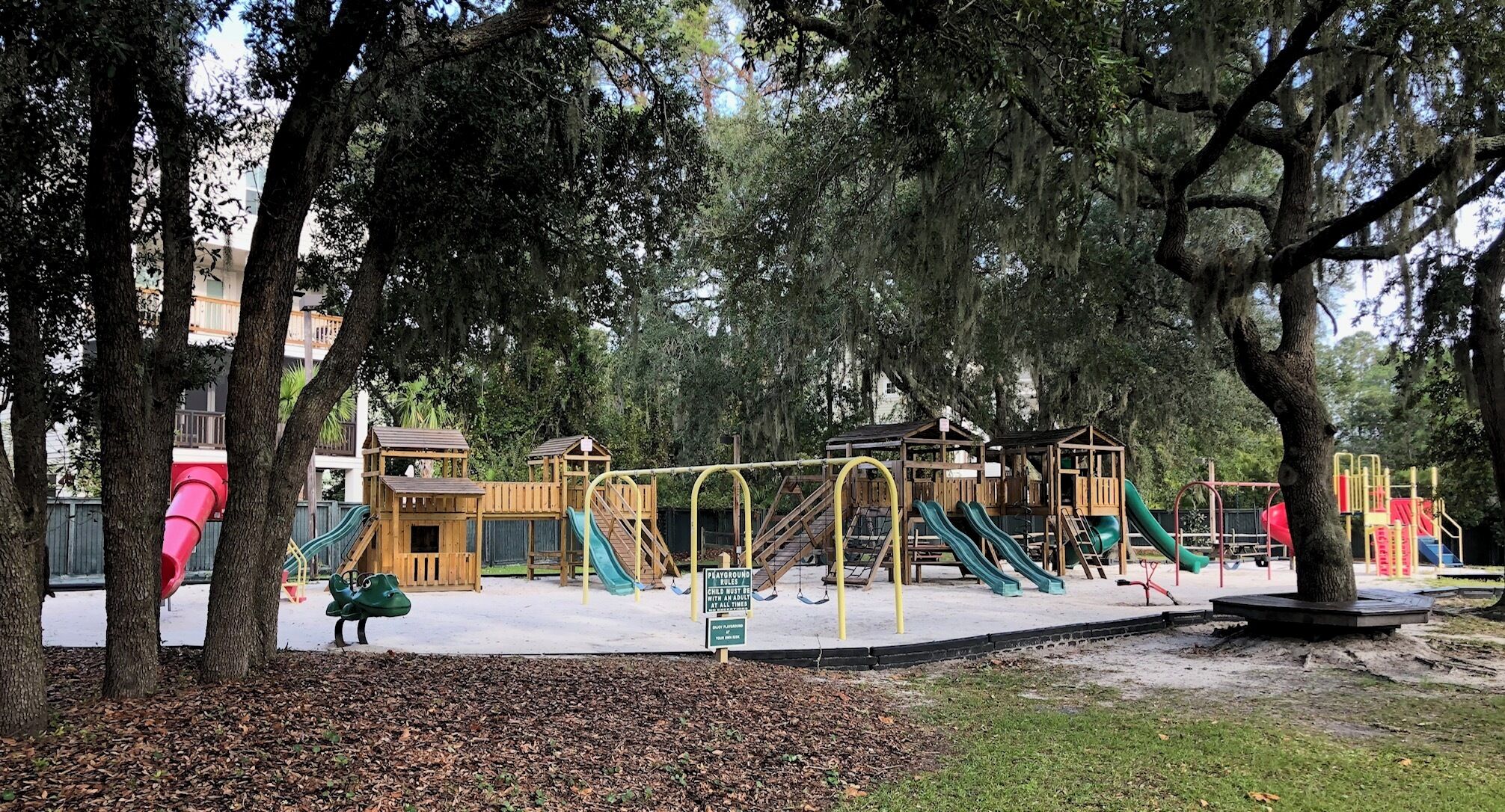 A playground with slides and climbing structures, surrounded by trees.