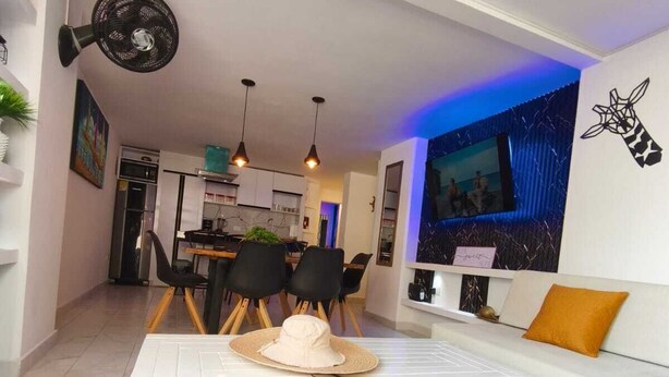Ein modernes Wohnzimmer mit einem weißen Sofa, einem Esstisch mit Stühlen und einer Küche im Hintergrund.