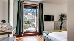 Ein Hotelzimmer mit Bett, Wandfernseher, Fenster mit Vorhängen, Heizkörper und Blick ins Freie.