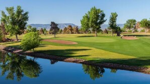 Un campo da golf con uno stagno che riflette gli alberi e il cielo.