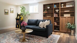 Un salon avec un canapé bleu foncé, une table basse ronde et une bibliothèque en bois remplie de livres et d’objets décoratifs.