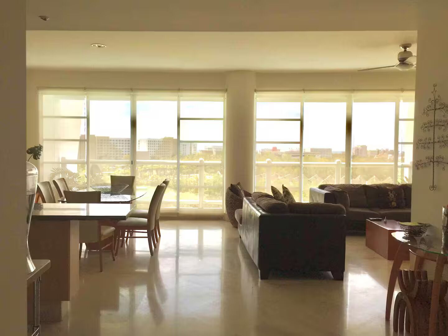 A spacious living area with a dining table, chairs, a sofa, and large windows offering a city view.