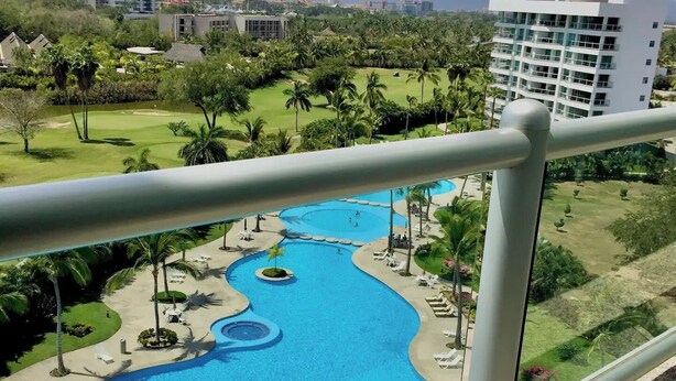 Ein Resort mit einem großen, gewundenen Pool, umgeben von Palmen und Liegestühlen.