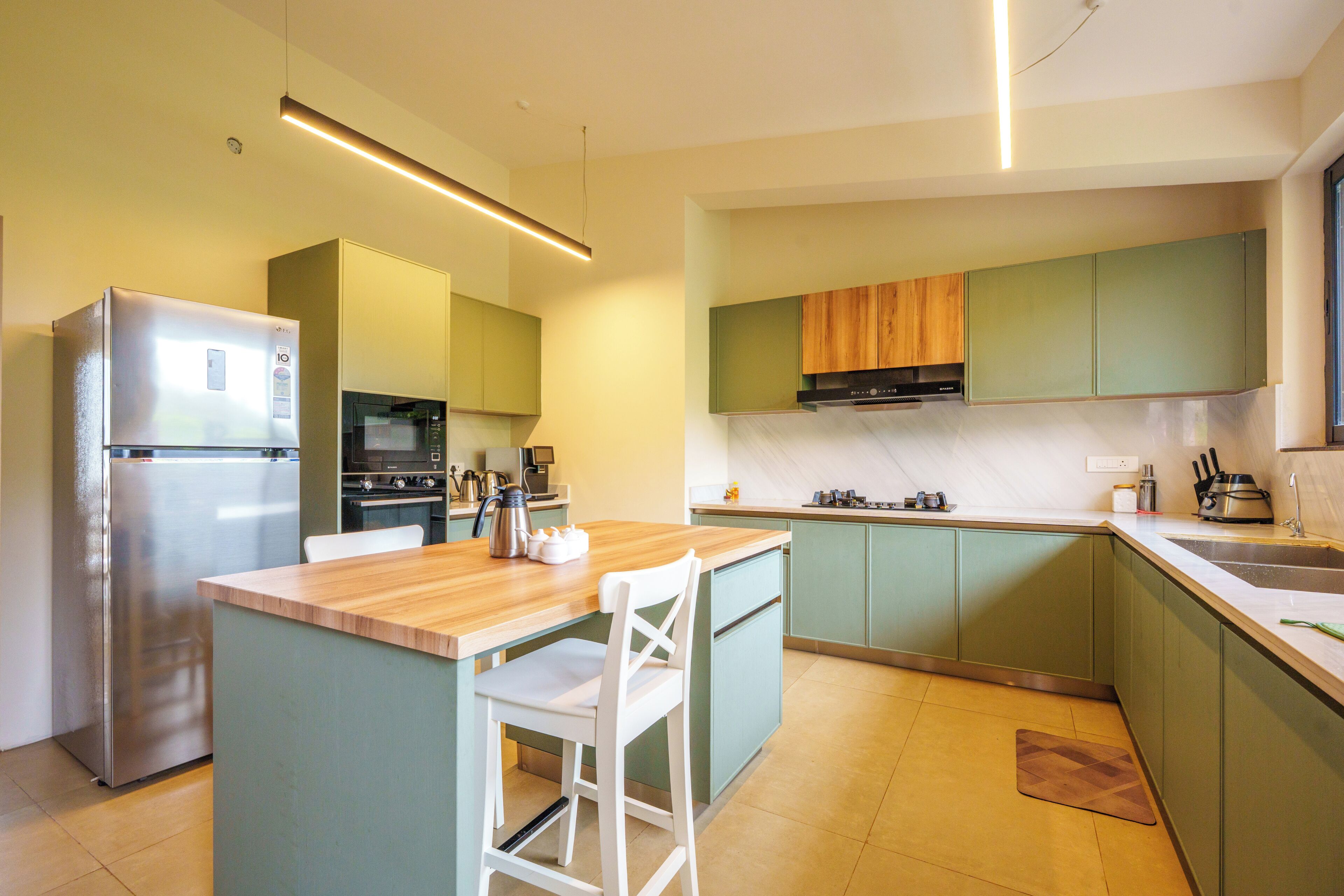 A modern kitchen with a central island, built-in appliances, and green cabinetry.