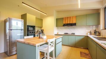 A modern kitchen with a central island, built-in appliances, and green cabinetry.