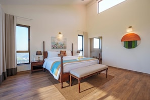 Une chambre spacieuse avec un grand lit, un banc, une table de chevet, une lampe et un tableau au mur.
