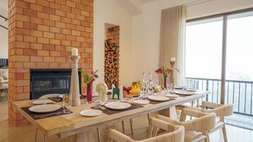 Un comedor con chimenea de ladrillo, una mesa larga dispuesta para seis personas y vistas al exterior.