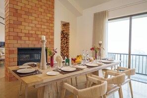 A dining area with a brick fireplace, a long table set for six, and a view of the outdoors. - amã Stays & Trails The Long House, Coonoor (Coonoor)