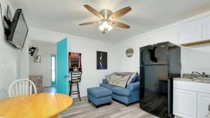 A compact living space with a dining area, a sofa, a refrigerator, and a ceiling fan.