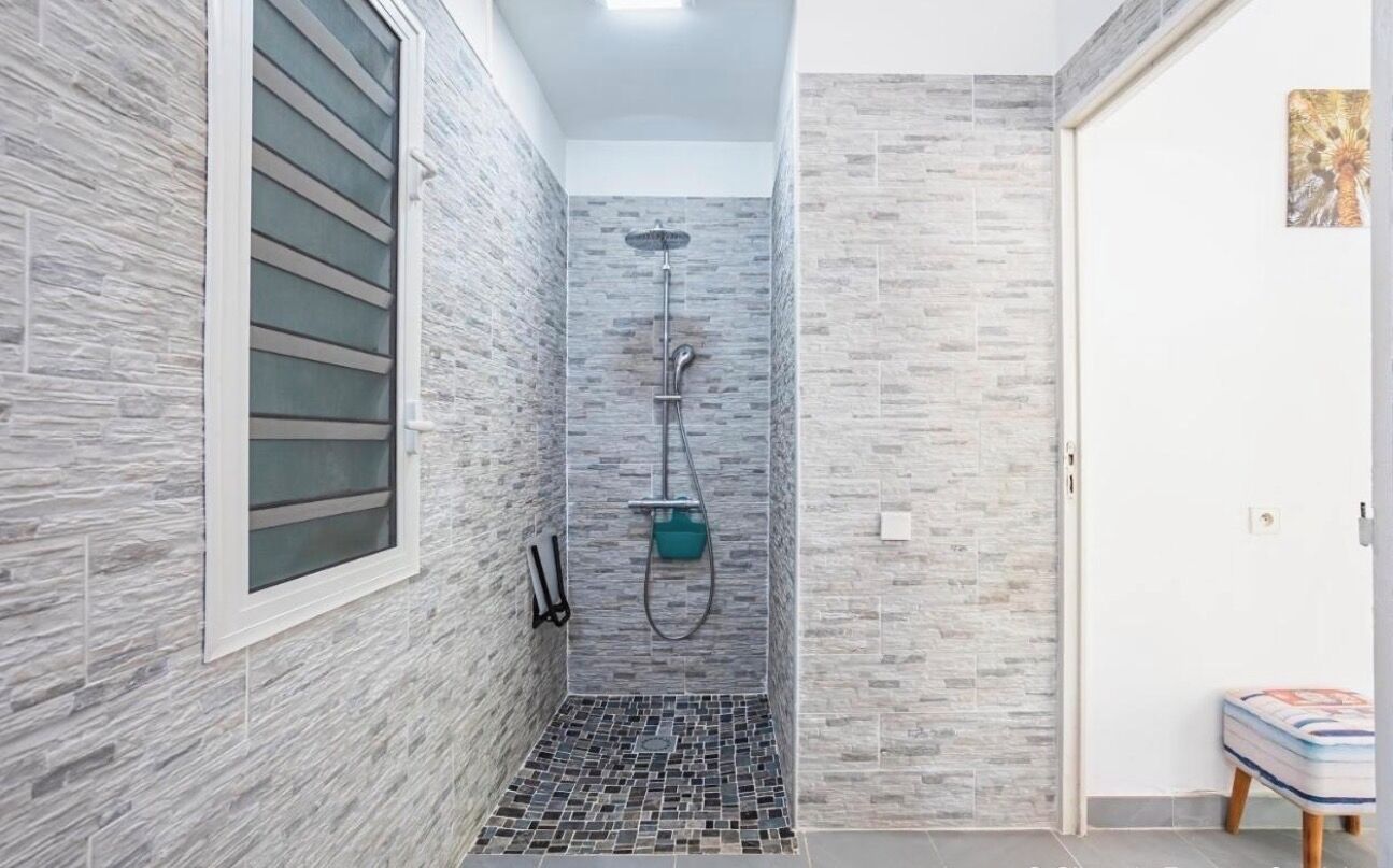 Ein Badezimmer mit Dusche, gefliesten Wänden, einem Fenster und einer kleinen Sitzbank.