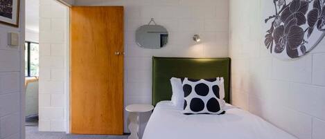 Een slaapkamer met een groen bekleden hoofdeinde, een witte spreidek en een ronde spiegel, plus een bloemendecoratie aan de muur.