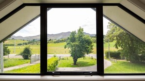 Una habitación con un gran tragaluz que ofrece vistas a un paisaje verde con colinas y un árbol.