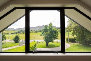A room with a large skylight window offering a view of a green landscape with hills and a tree. - Coronet Peak View | 3BR Home with Hot Tub & Garden (Queenstown)