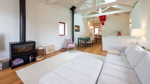 Uma sala de estar moderna com lareira, um sofá, um espaço de refeições e uma cozinha ao fundo.