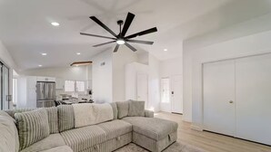 Ein geräumiges Wohnzimmer mit einer großen Eckcouch, einem Deckenventilator und einer Küche im Hintergrund.
