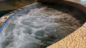 Ein Whirlpool mit blauer Kante, umgeben von einer Betonterrasse, im Hintergrund ein Gebäude mit Lichterketten.