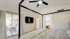Ein Schlafzimmer mit Bett, Deckenventilator, Fernseher und einem Badezimmer mit Spiegel und Waschbecken.