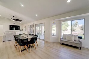 A spacious living area with a dining table, black chairs, a grey sofa, and large windows offering a view of the outdoors. - Modern Retreat with Private Pool/Hot Tub! (Mesa)