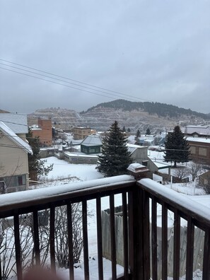 A snowy residential area with houses, a wooden fence, and a distant hill.