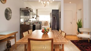 A dining area with a wooden table, wicker chairs, a fruit bowl, and a modern chandelier. - OPEN SPACE premium in the Gardens (São Paulo)
