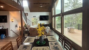 A dining area with a wooden table set for six, surrounded by chairs. A chandelier hangs from the ceiling, and a large window offers a view of the outdoors. - Bear House in the mountains Cuchara Co. (La Veta)