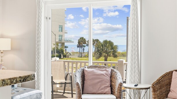 Une pièce avec vue sur un balcon, une chaise en osier, une petite table et une lampe.