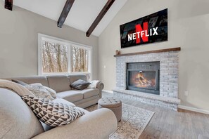 A living room with a beige sofa, a fireplace, and a Netflix sign on the wall. - Calm Waters w/ Hot Tub, Game Room & Patio (Lake Ariel)
