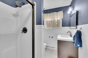 Ein Badezimmer mit Dusche, Toilette, Waschbecken und einem Fenster mit Vorhang.