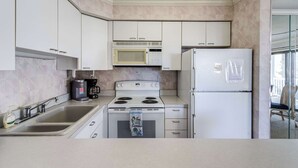 Una cocina con gabinetes blancos, estufa, microondas y refrigerador.