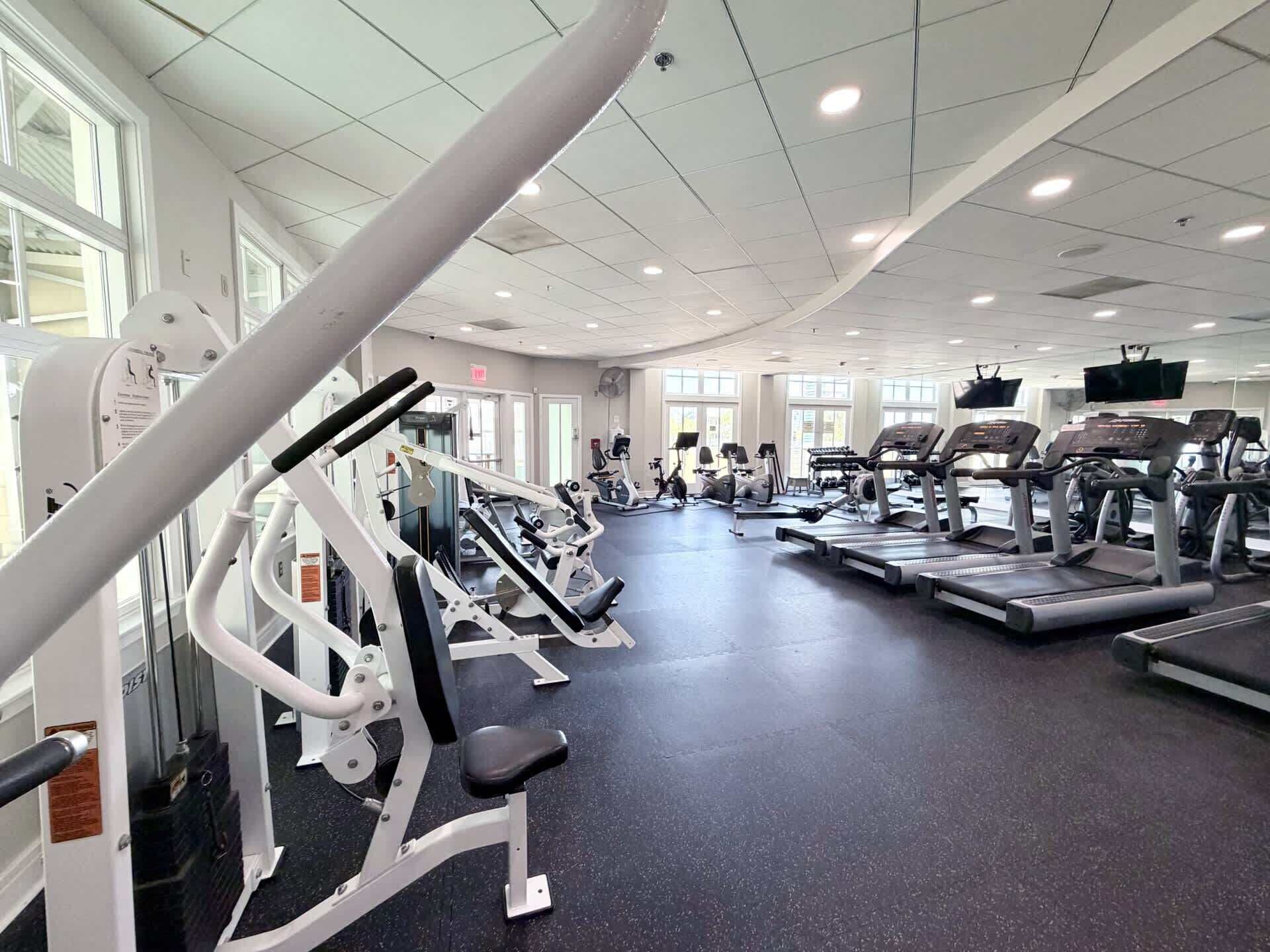 A gym with various exercise machines, large windows, and a ceiling with recessed lighting.
