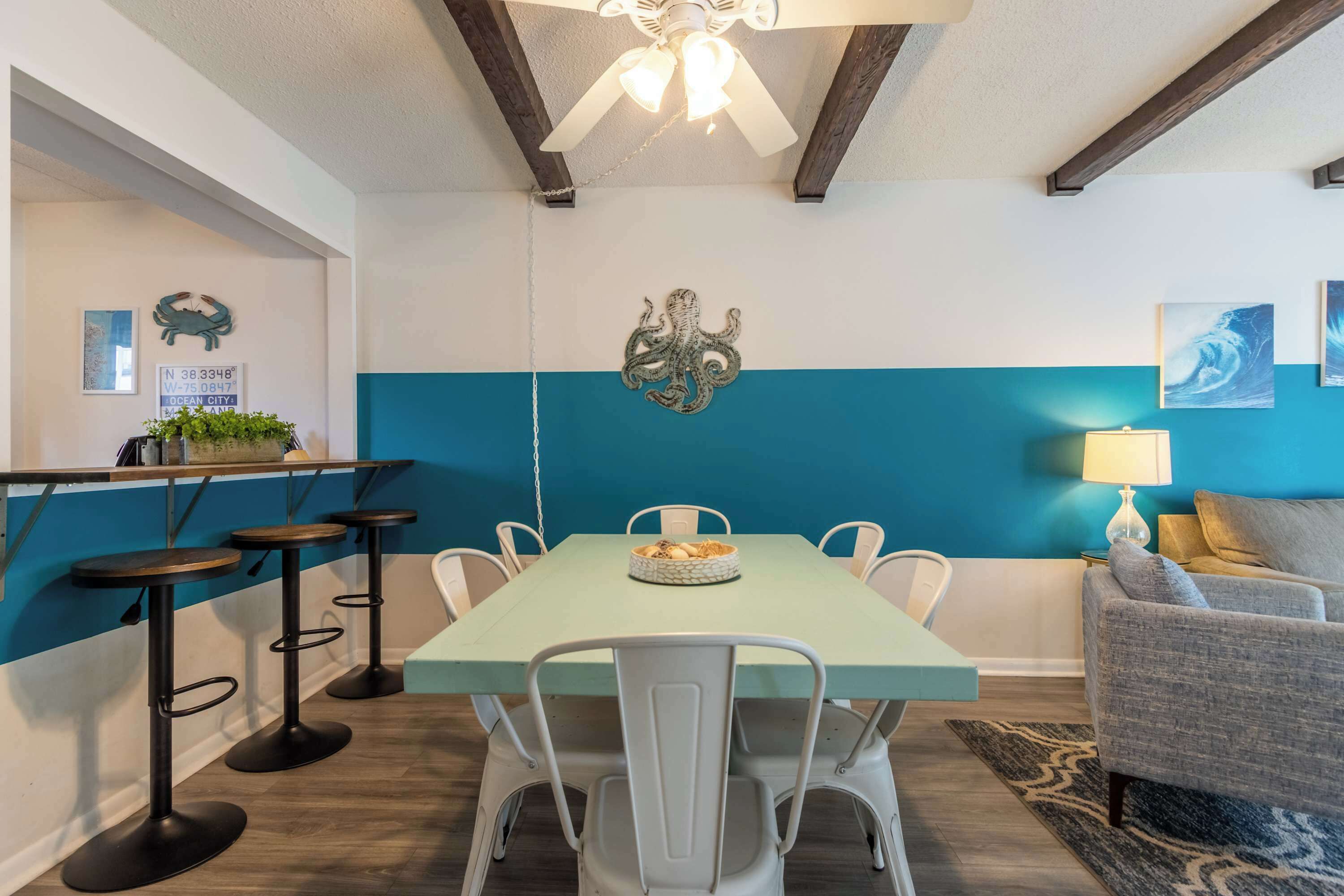 A dining area with a teal-colored table, white chairs, and a ceiling fan.