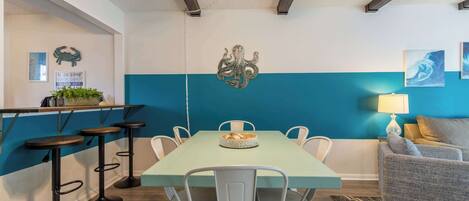 A dining area with a teal-colored table, white chairs, and a ceiling fan.
