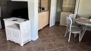 Uma cozinha compacta com televisão, móveis de vime branco e uma área de refeições com mesa e cadeiras.