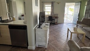 Sala de estar com sofá, mesa de centro, área de jantar com cadeiras, cozinha com lava-louças e ventilador de teto.