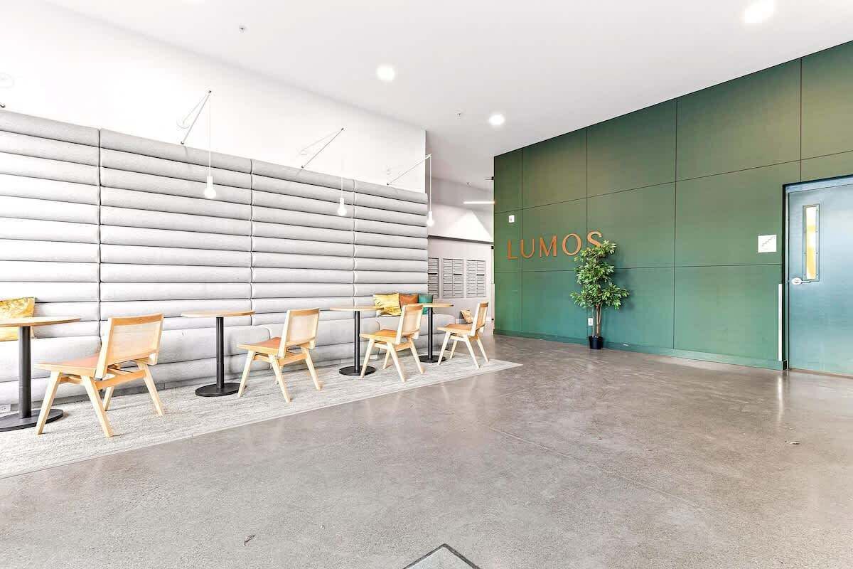 Bright and minimalist lobby featuring sleek seating areas, wood-accented tables, and a modern green wall with the “Lumos” sign, creating a stylish first impression.