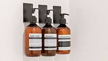 Three bottles of body wash, shampoo, and conditioner on a wall-mounted dispenser.