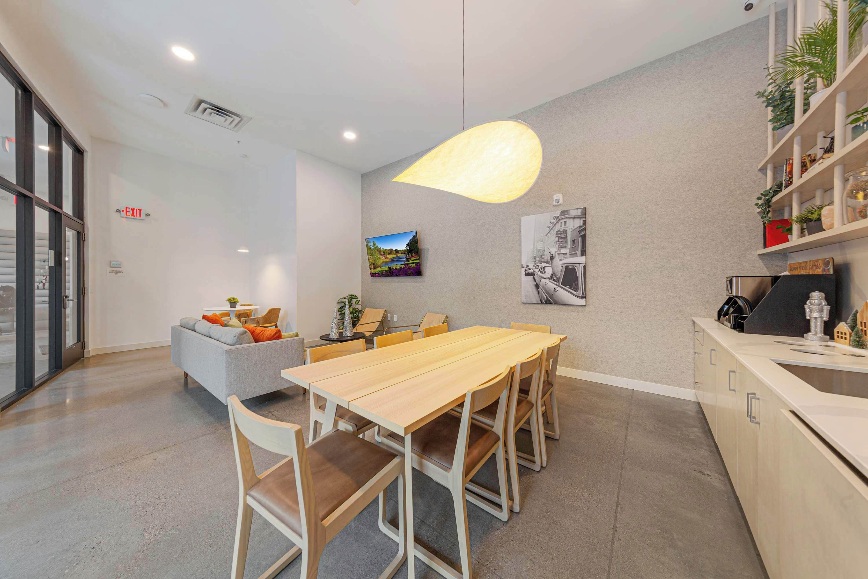 Une salle de réunion moderne, dotée d’une longue table, de chaises, d’un canapé et d’une étagère murale agrémentée de plantes.