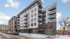 Un edificio de apartamentos de varios pisos con balcones, un estacionamiento y suelo cubierto de nieve.