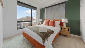 Une chambre d’hôtel moderne avec un grand lit, deux tables de chevet, une vue sur la ville et un mur d’accent de couleur verte.