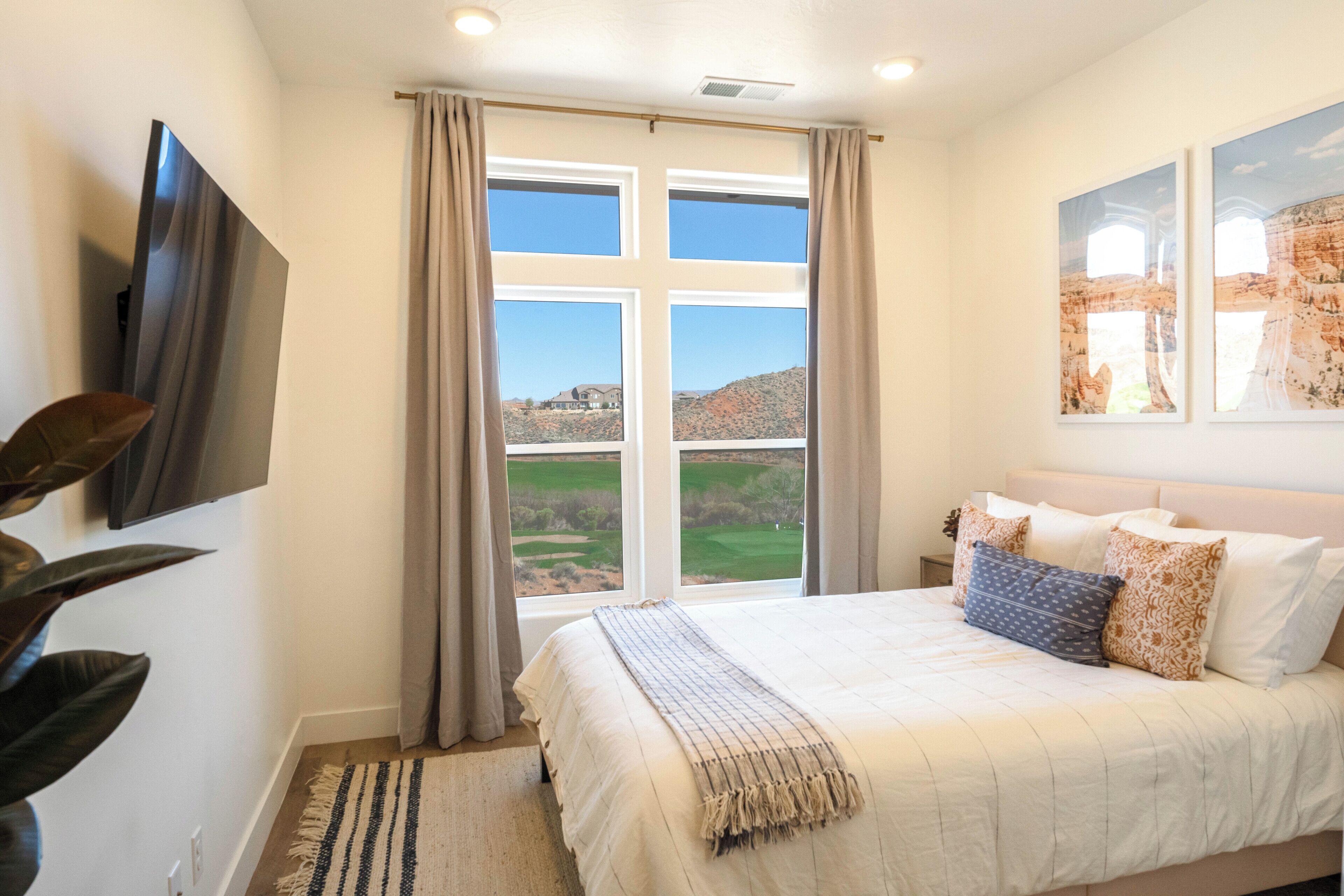 A bedroom with a large bed, a flat-screen TV, a view of a golf course, and a painting on the wall.